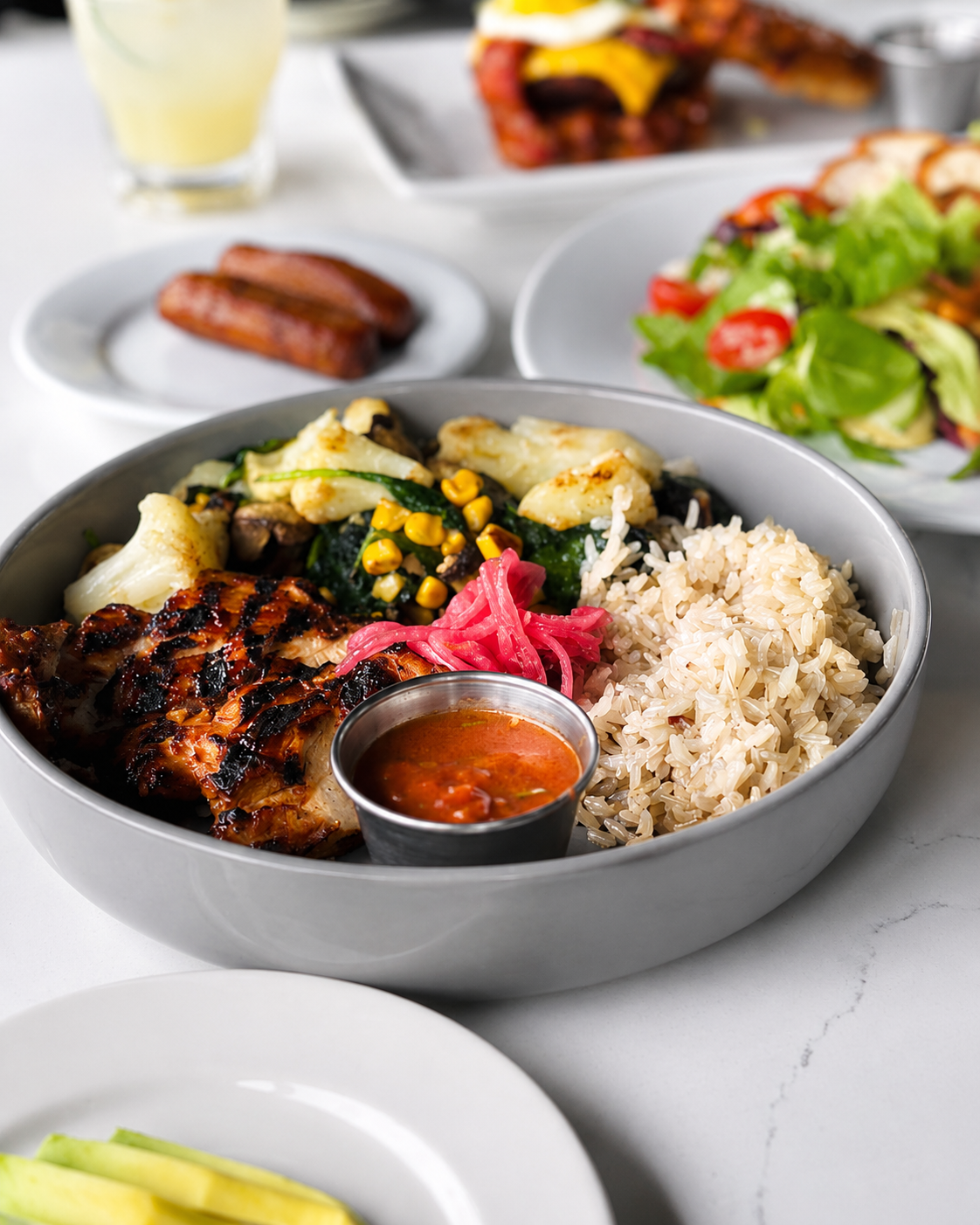 A bowl of grilled chicken, brown rice, cauliflower, spinach, roasted corn and pickled red onions with a side of salsa.