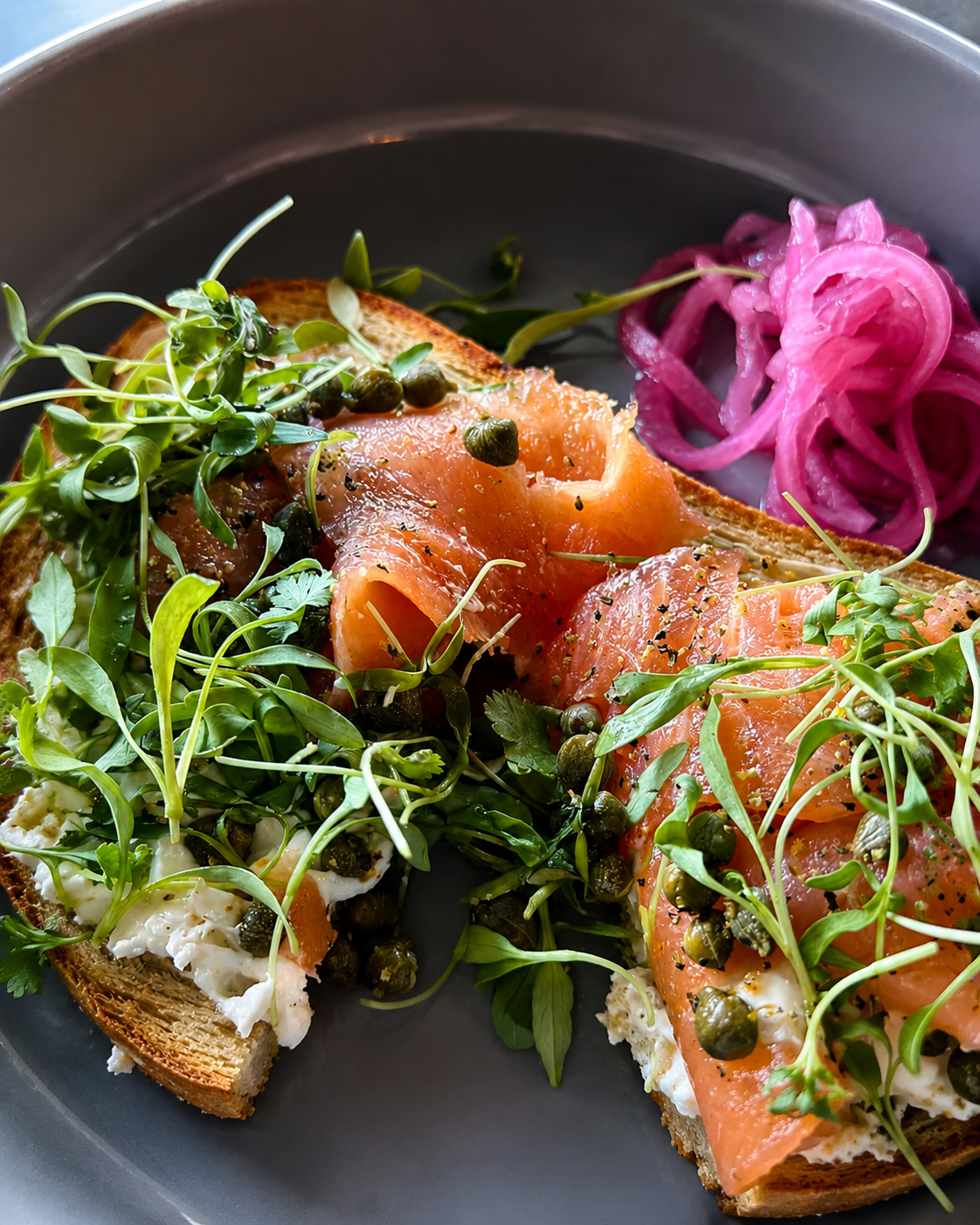 Open-faced toast with cream cheese, smoked salmon, capers, fresh greens and pickled red onions.