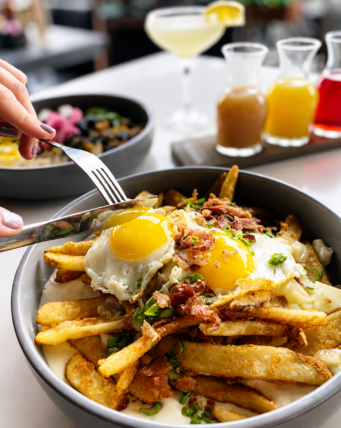 Crisp potato wedges topped with two fried eggs, bacon, scallions, cheese and gravy at a brunch table.