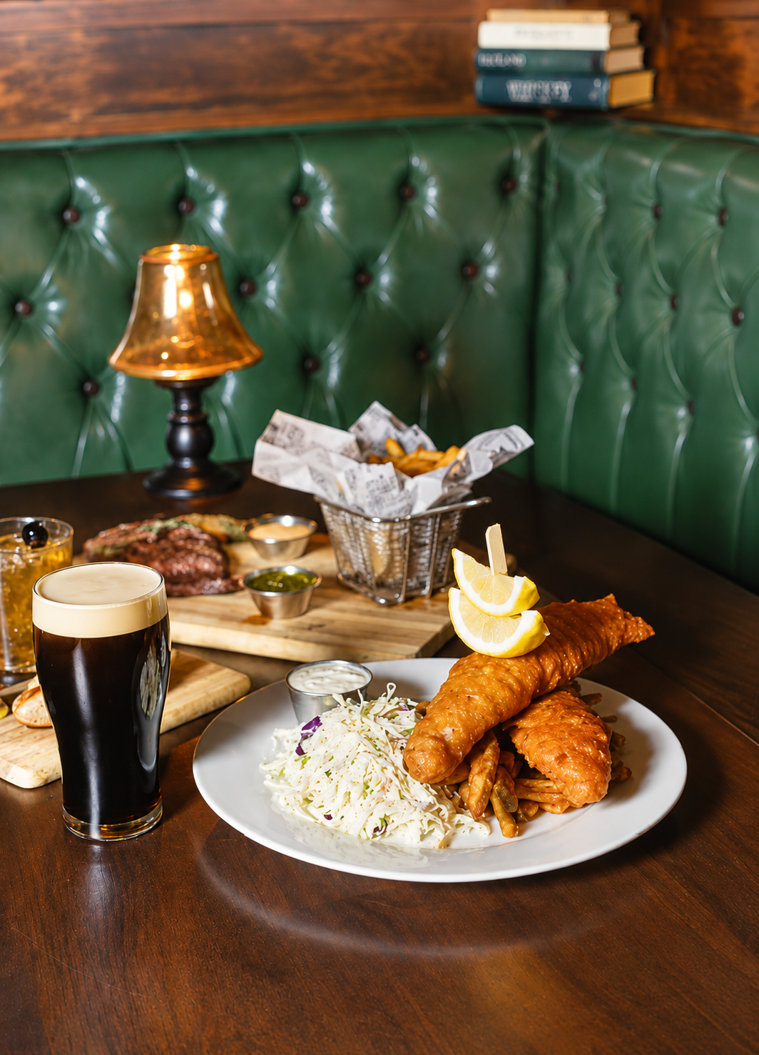 A green leather booth inside Patrick Molloy's with fish and chips on the table and guests filling the bar behind it.