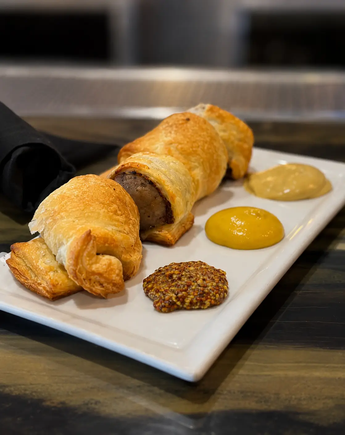 A golden puff-pastry Irish sausage roll sliced open on a board with a side of dijon mustard.
